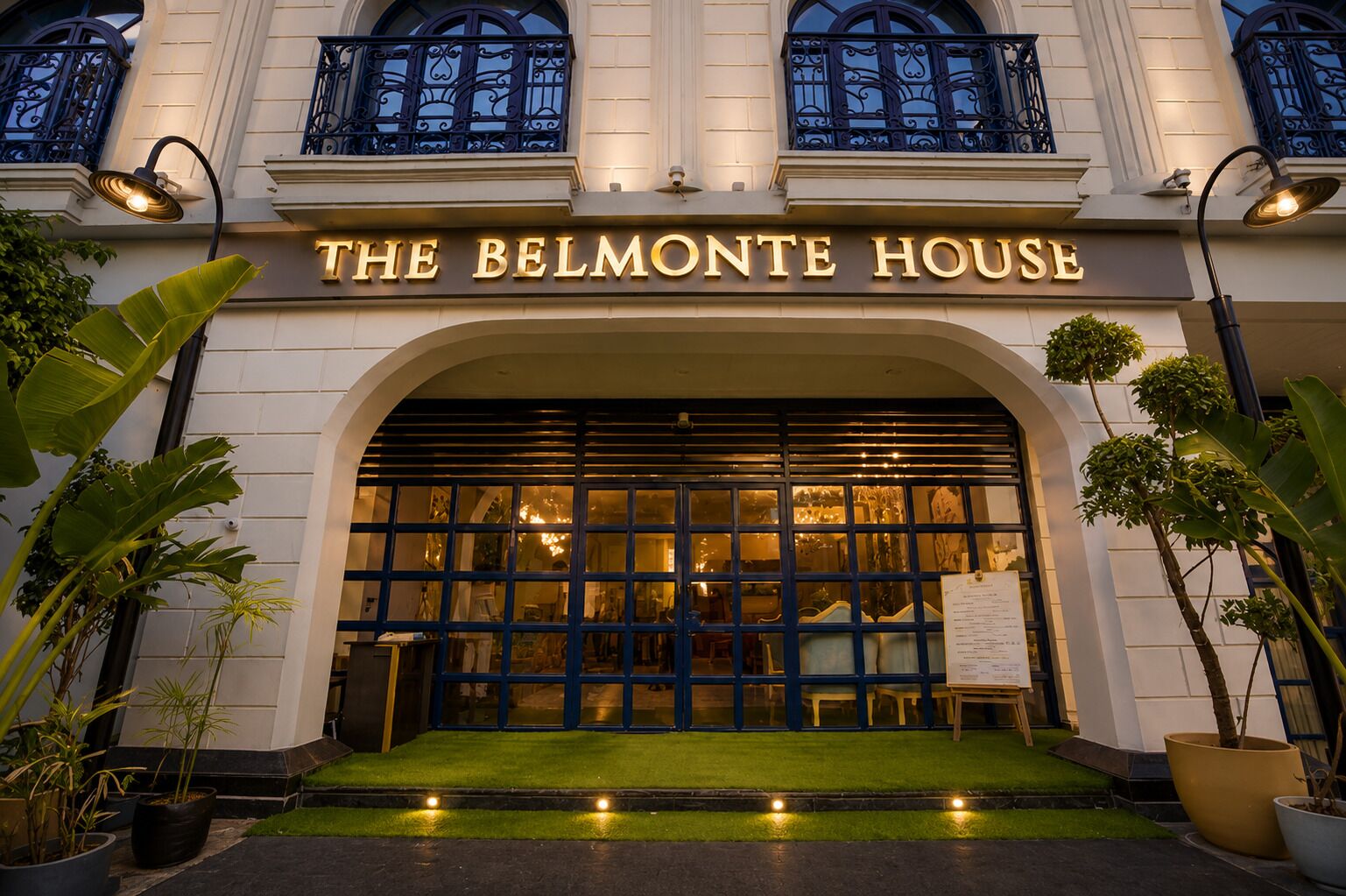 De ingang van House Belmonte met een grote gewelfde deuropening, potplanten en een bord boven de ingang.