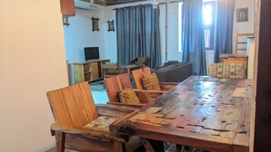 A dining area with a long wooden table, several chairs, a sofa, and a television in the background. - Elegant Zanzibar City Apartment Comfort and Convenience Await (Zanzibar Town)