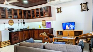 A living room with a sofa, wooden chairs, a television, and a kitchen area with cabinets and a microwave. - Elegant Zanzibar City Apartment Comfort and Convenience Await (Zanzibar Town)