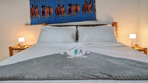 A hotel room with a large bed, white bedding, a blue tapestry with figures, two bedside lamps, and a grey throw blanket. - Elegant Zanzibar City Apartment Comfort and Convenience Await (Zanzibar Town)