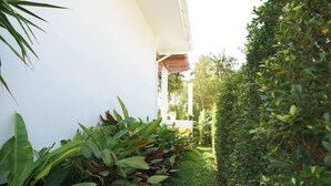 A narrow pathway flanked by lush greenery and a white building. - O3 Green 2b Garden Pool Villa and Unique Furniture (Ko Pha-ngan)