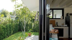 A modern kitchen with a view of a lush garden, a dining area with a table and chairs, and a large window. - O3 Green 2b Garden Pool Villa and Unique Furniture (Ko Pha-ngan)