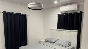 A bedroom with a bed, curtains, a nightstand, and an air conditioning unit.