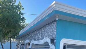 A modern building with a blue and white facade, a gated entrance, and a small garden area with plants.