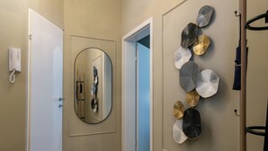 A hallway with a round woven rug, a round ottoman, a wall-mounted mirror, and a decorative wall piece. - Quiet apartment 6 min walk to metro - 4 stops to Opera (Wien city)