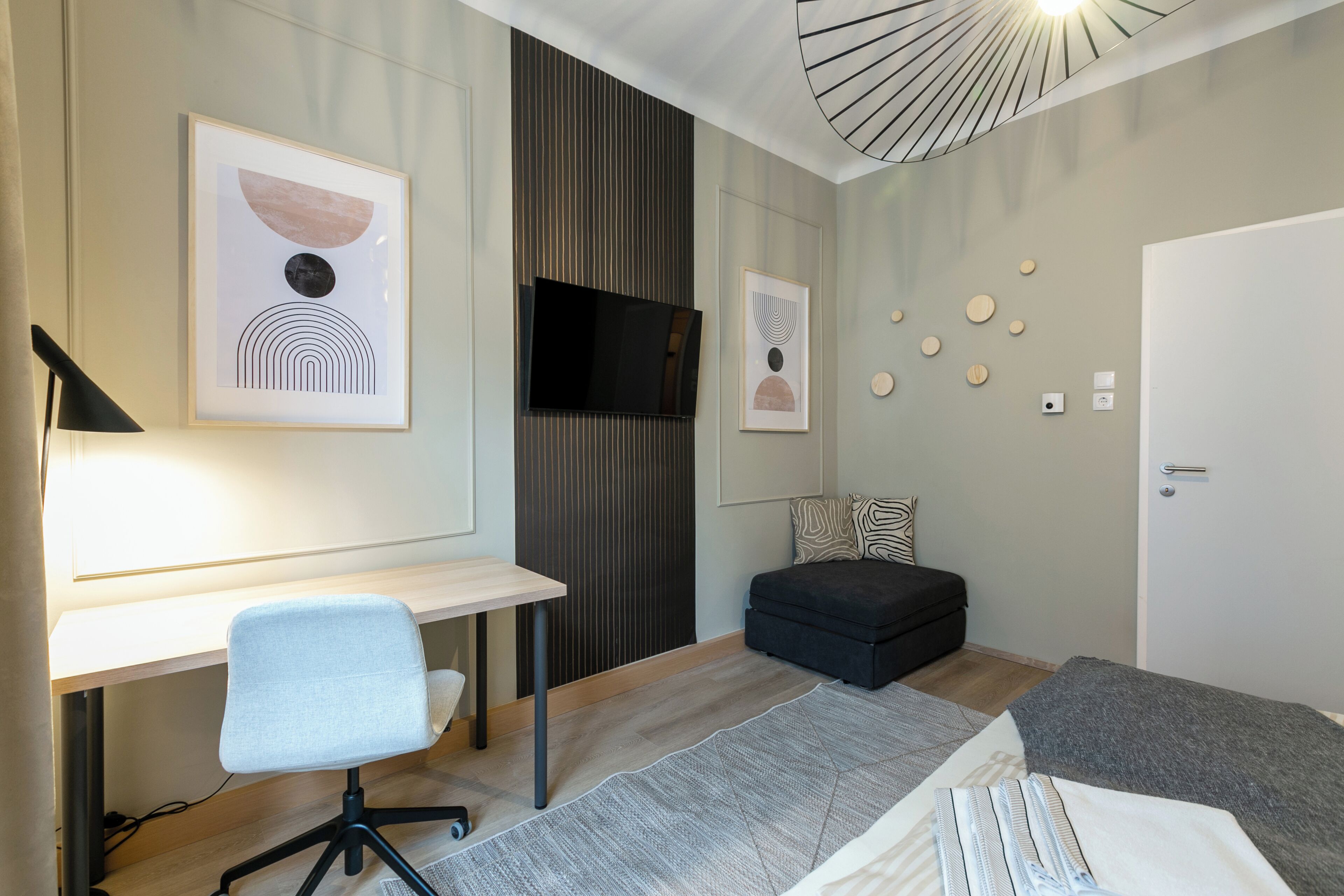 A modern hotel room with a desk, chair, sofa, and a bed.