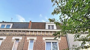 A two-story brick building with a blue door, stone steps, and a small window. - Anavel Atao (Lille)