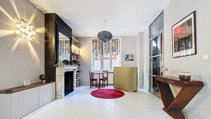 A modern kitchen with a fireplace, a dining area with a red rug, and a wooden console table. - Anavel Atao (Lille)