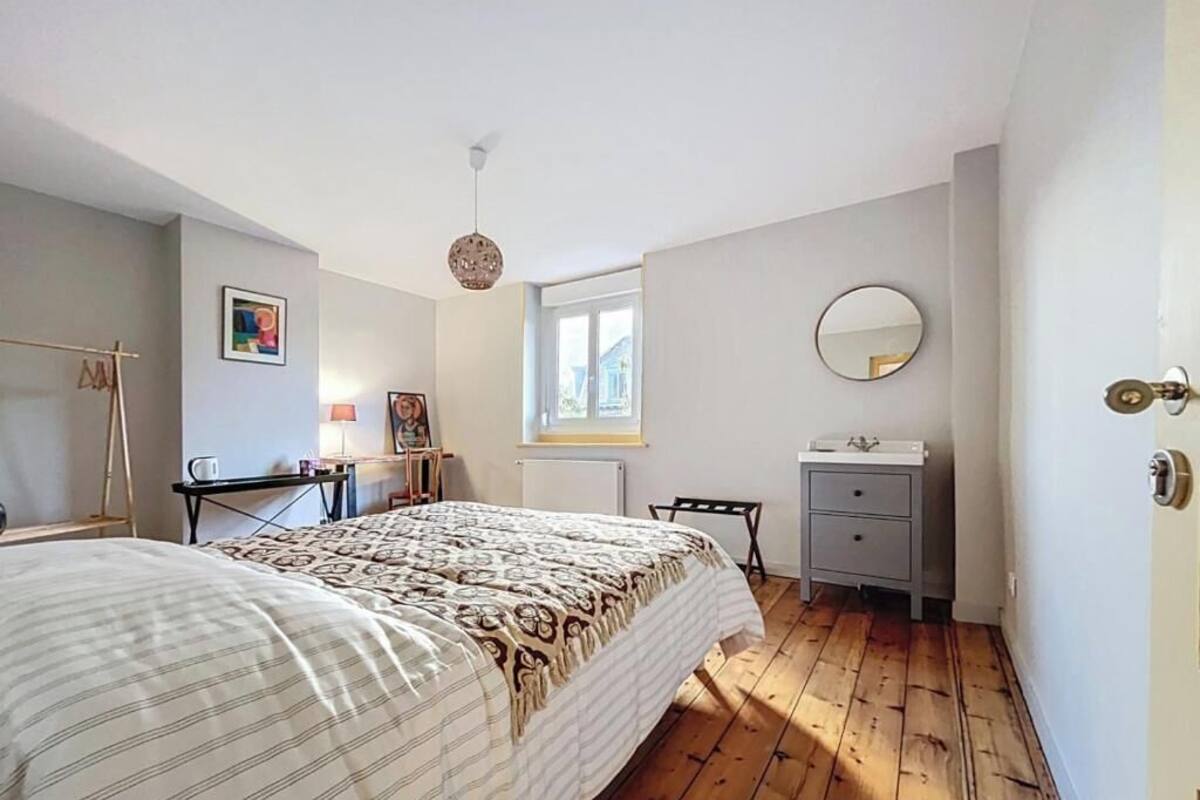 A bedroom with a bed, a bedside table, a dresser, a mirror, a window, and a door.