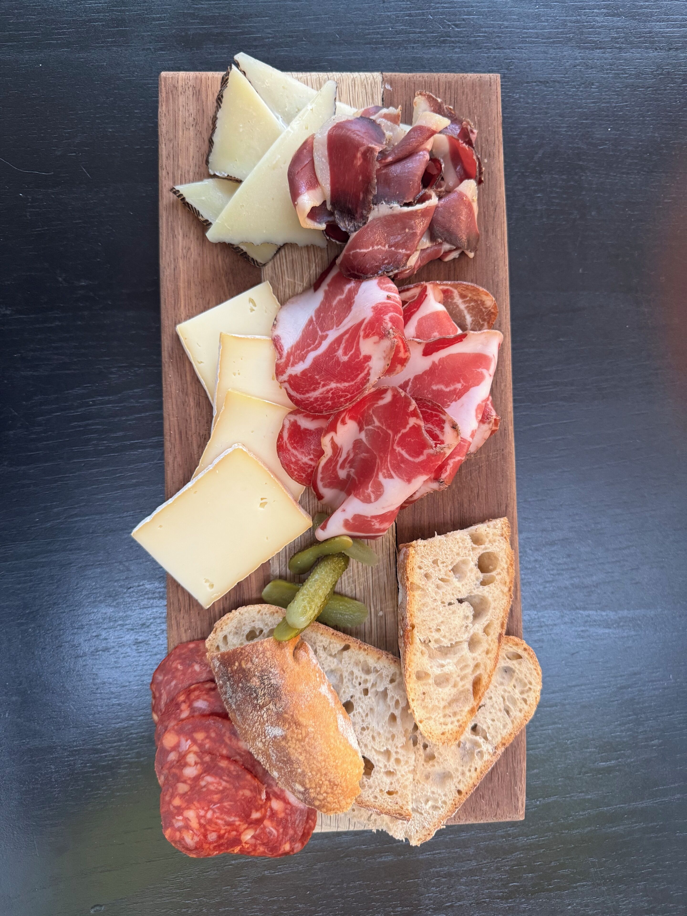 Un tagliere con diversi formaggi, salumi, sottaceti e pane.