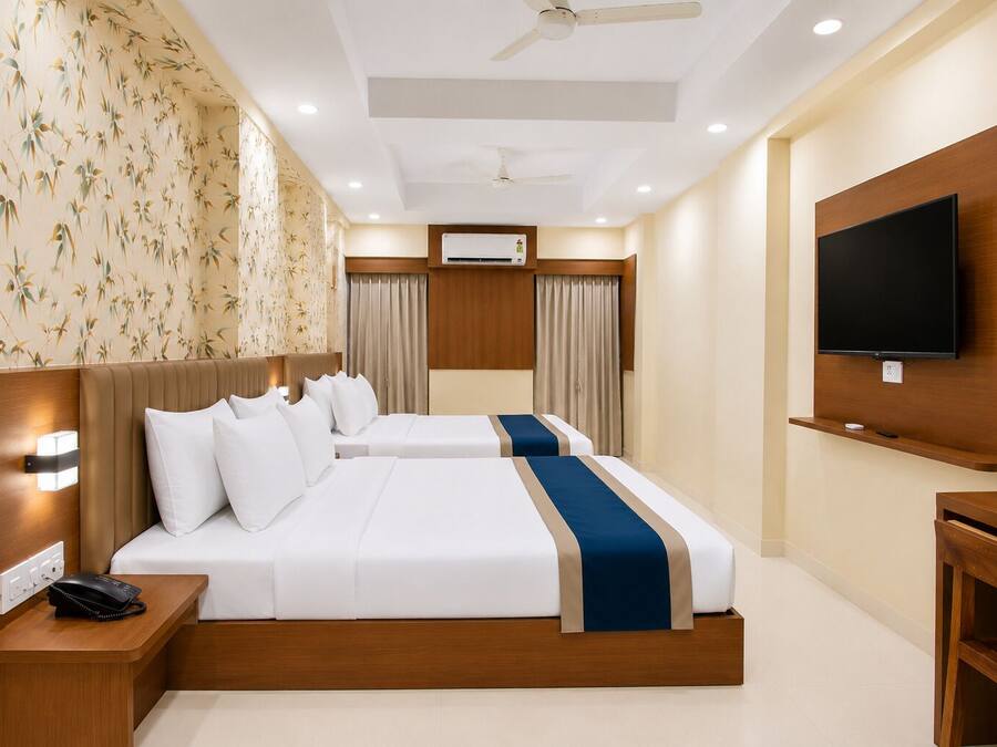 Quarto de hotel com cama, mesas de cabeceira, televisão, telefone e ventoinha no teto.