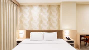Ein Hotelzimmer mit einem Bett, zwei Nachttischen, einem Schreibtisch, einem Sessel und einer Wand mit Muster.