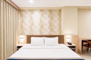 Habitación de hotel con cama, dos mesitas de noche, un escritorio, una silla y un papel tapiz estampado.