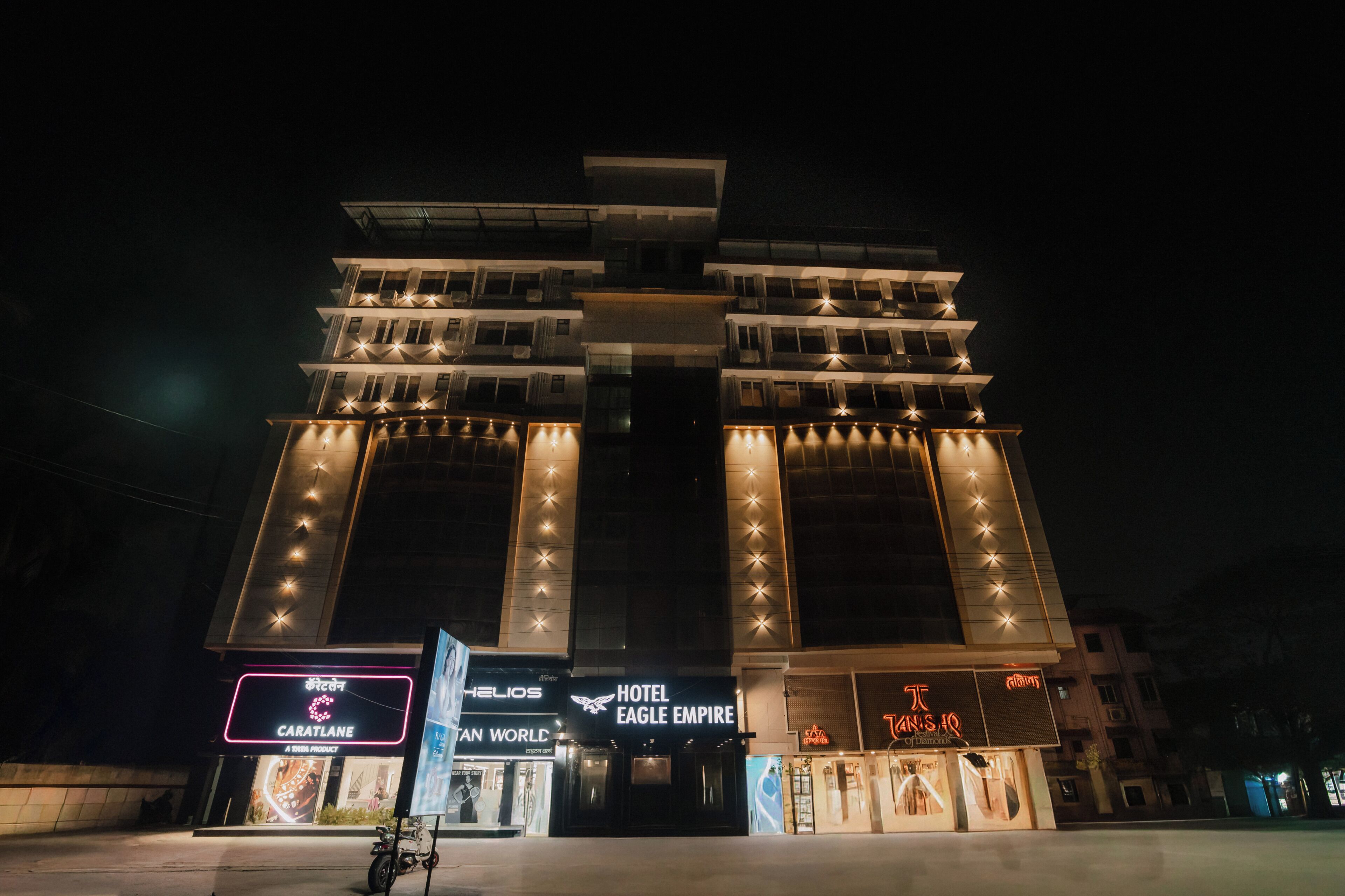 Ein mehrstöckiges Hotel mit beleuchteter Beschilderung, darunter 'Hotel Eagle Empire' und 'Caratlane'.