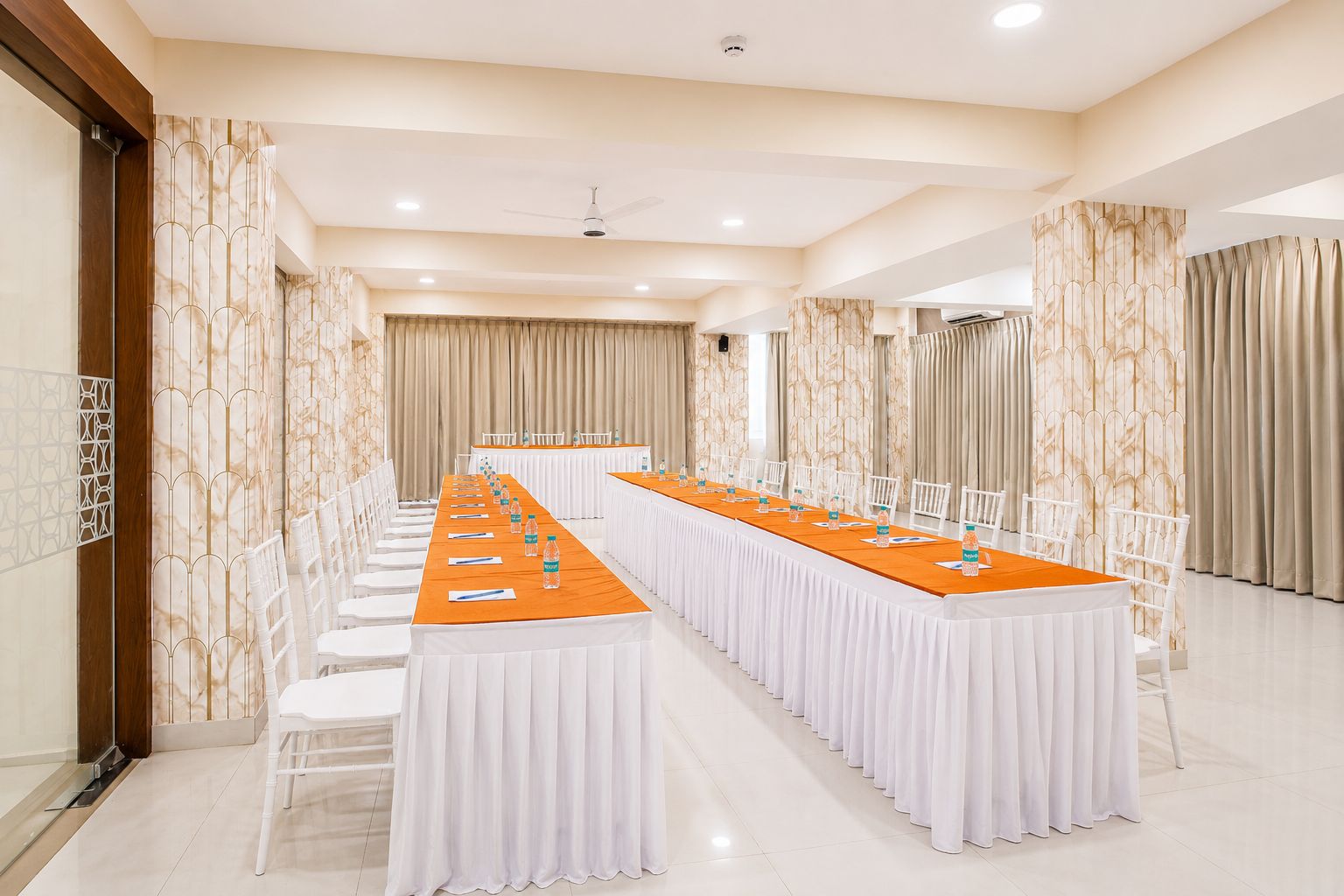A conference room with a long table, white chairs, and a ceiling fan.
