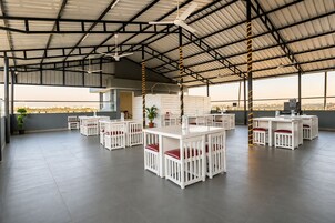 Un amplio espacio exterior con mesas blancas y sillas rojas acolchadas, un ventilador de techo y vistas a la ciudad.