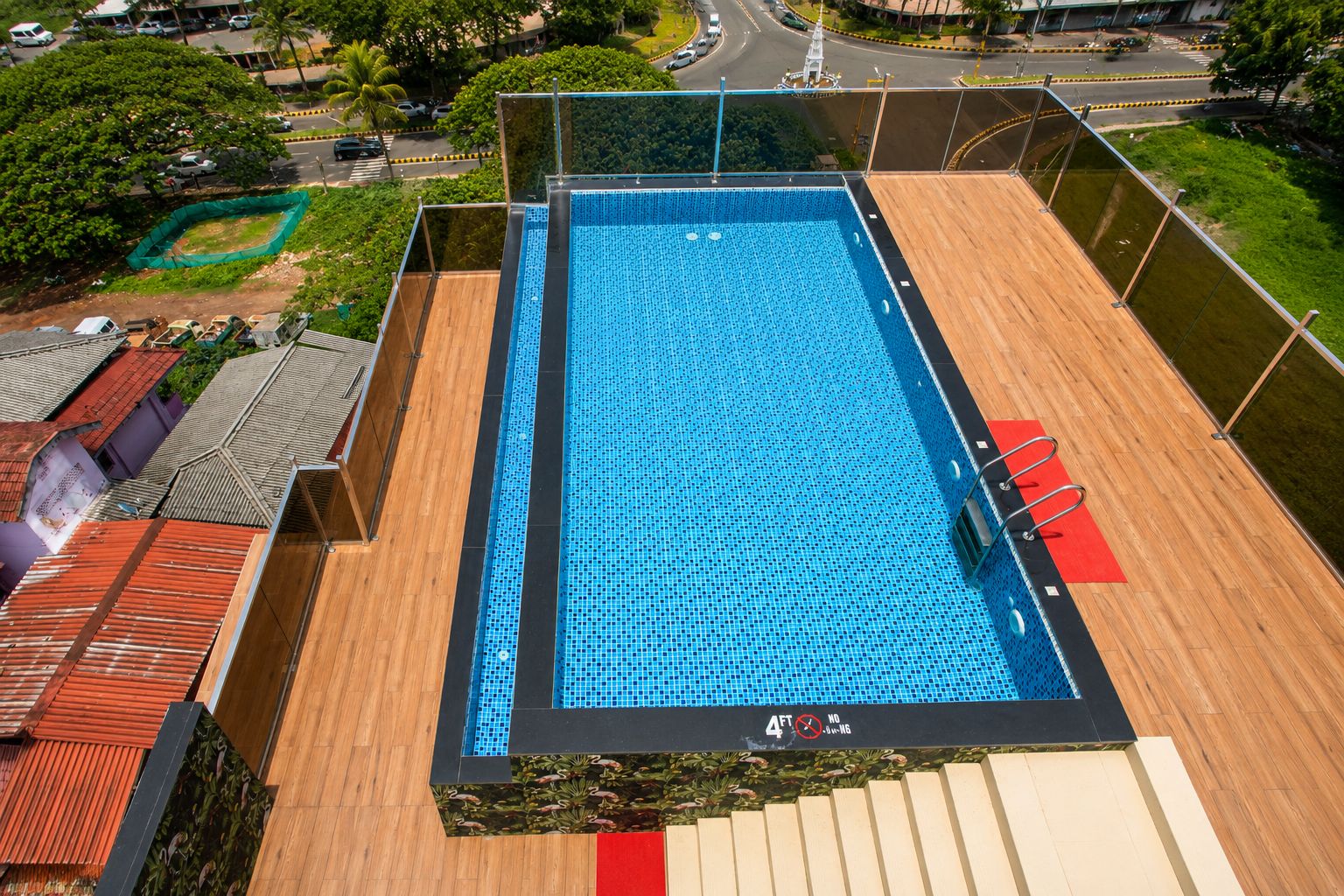 Vista aérea de una piscina en la azotea con cubierta de madera, rodeada de vegetación y edificios residenciales.