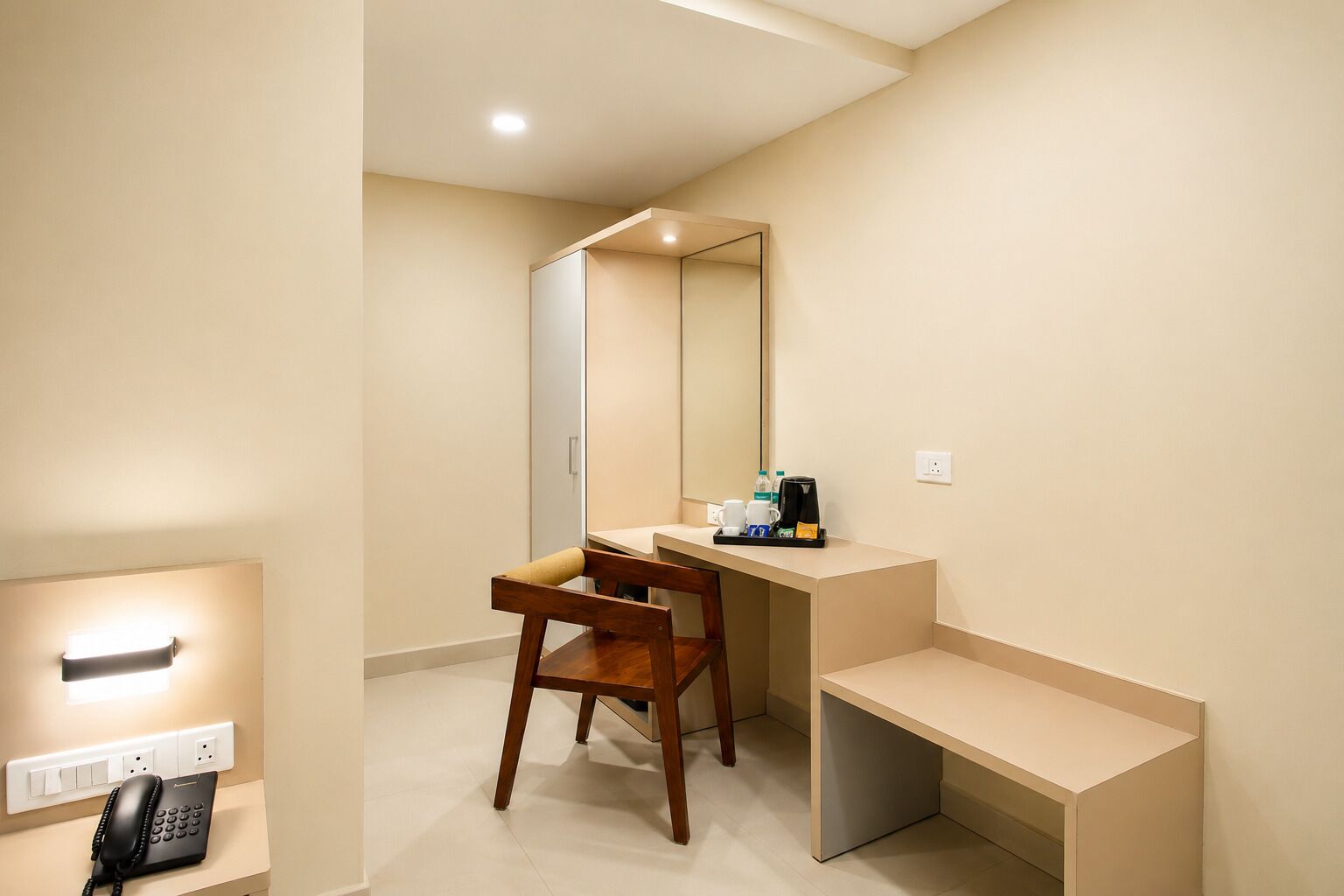 A hotel room with a wooden desk, a mirror, a telephone, and a coffee maker on the counter.