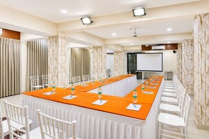 Una sala de conferencias con una larga mesa, sillas blancas y una pantalla para proyector.