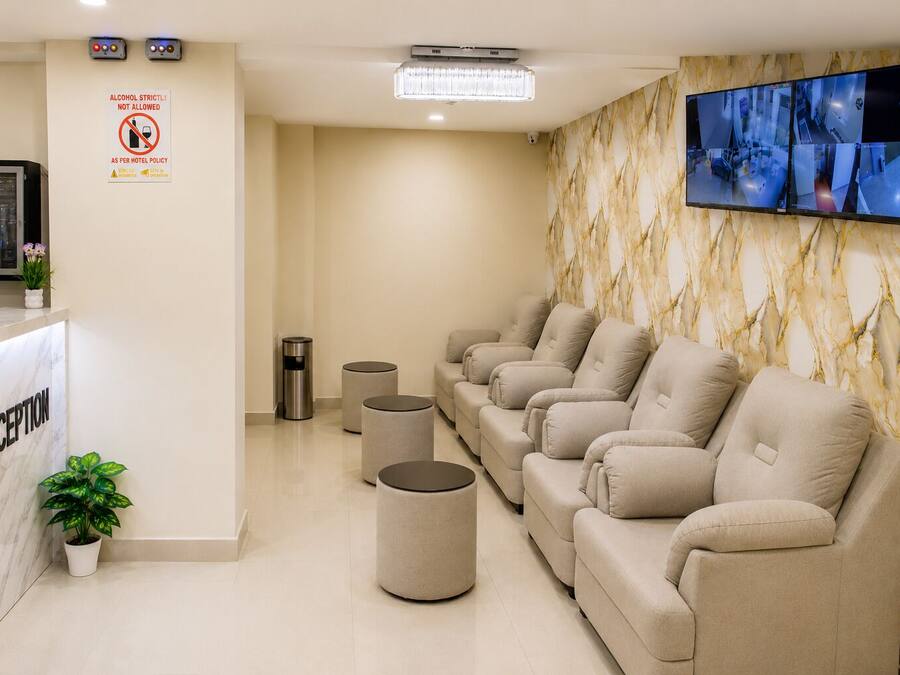 Zona de recepción con pared de mármol, mostrador de recepción, área de descanso con sillones de masaje, un cesto de basura y una cámara de seguridad.