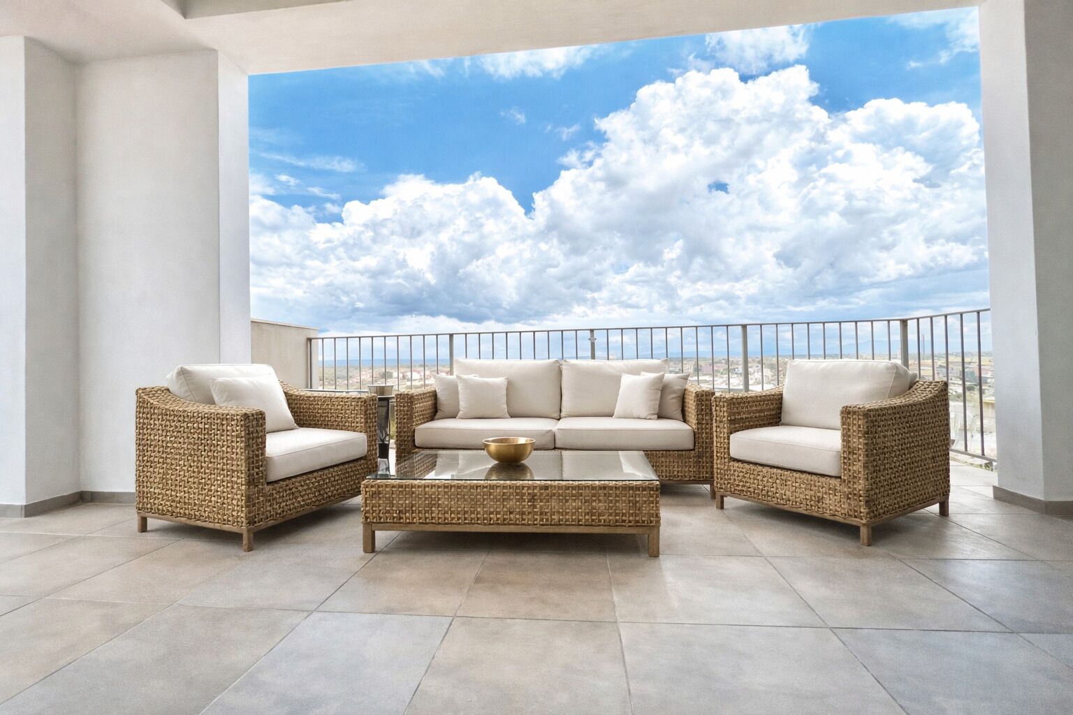 A balcony with wicker furniture, a glass coffee table, and a view of the sky and clouds.
