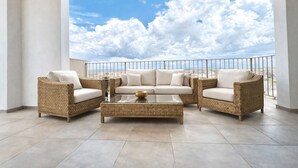 Un balcón con mobiliario de mimbre, una mesa de centro de vidrio y vistas al cielo y nubes.
