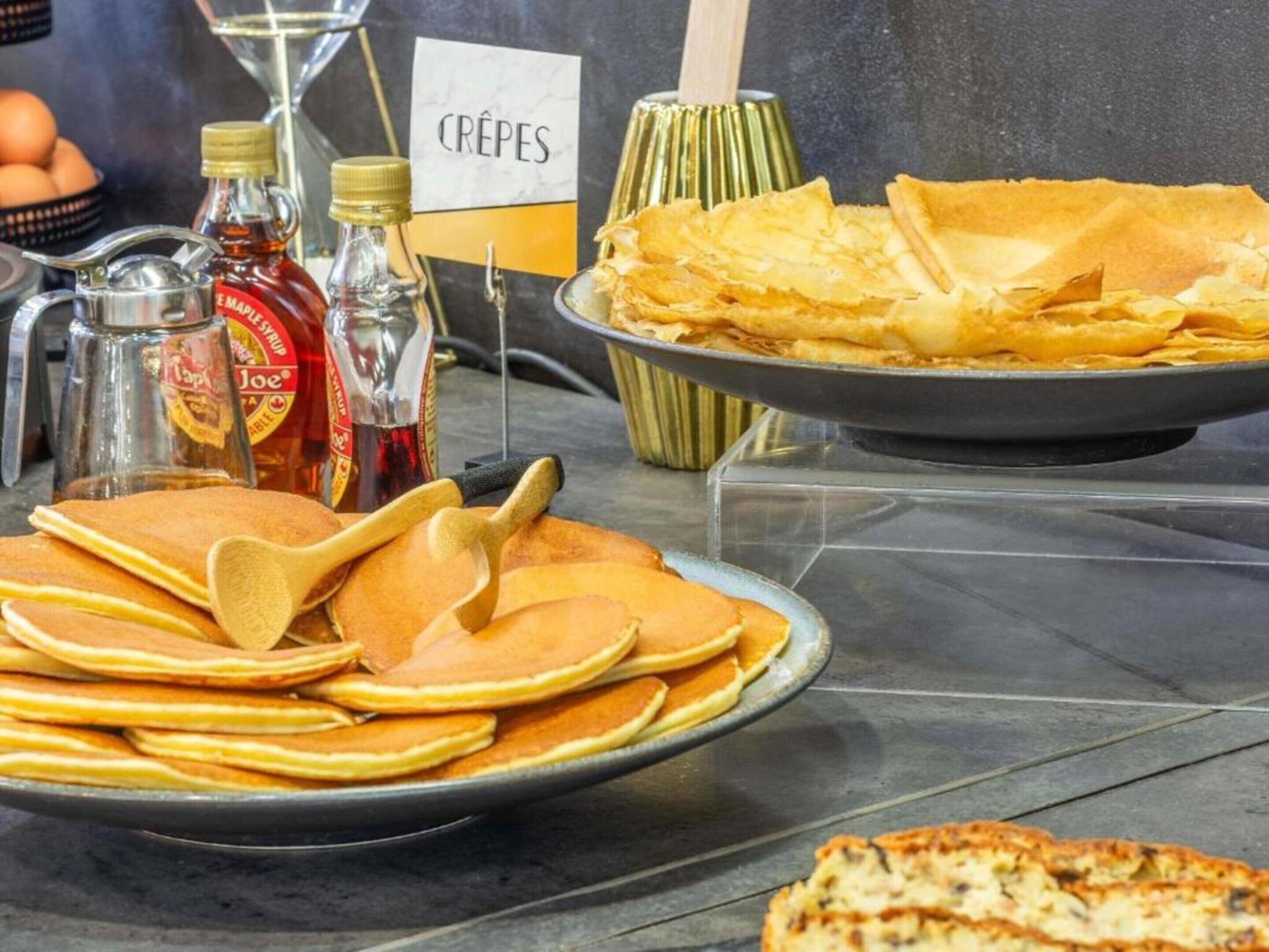A breakfast buffet with pancakes, crepes, and syrup bottles.