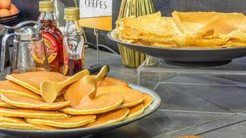 A breakfast buffet with pancakes, crepes, and syrup bottles.