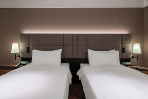 Habitación de hotel con dos camas, cabecero acolchado, lámparas de noche y mesitas de noche con teléfono.