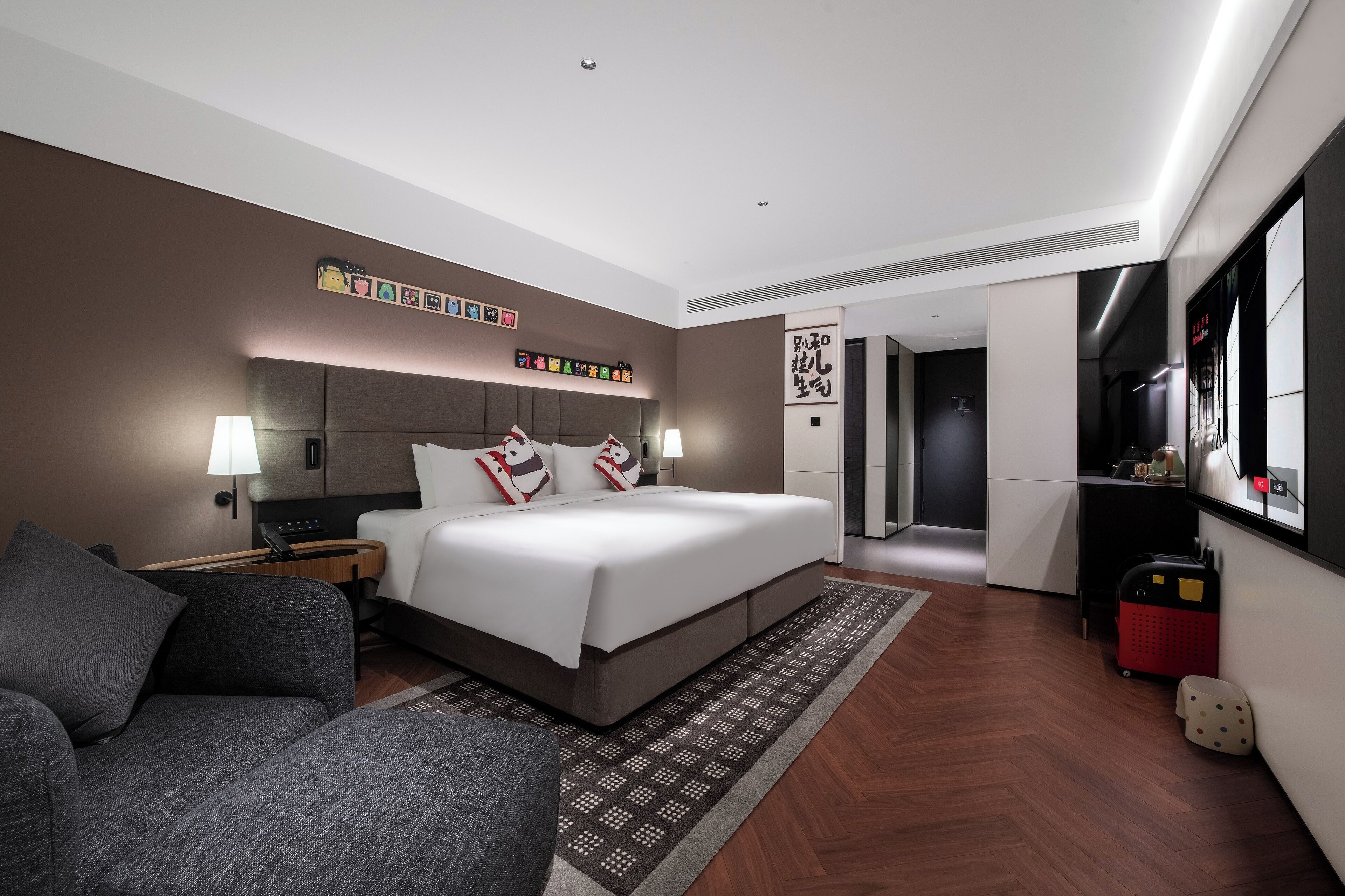 Una habitación de hotel moderna con una cama grande, mesitas de noche, un sofá, un tapete estampado y una pared decorada.