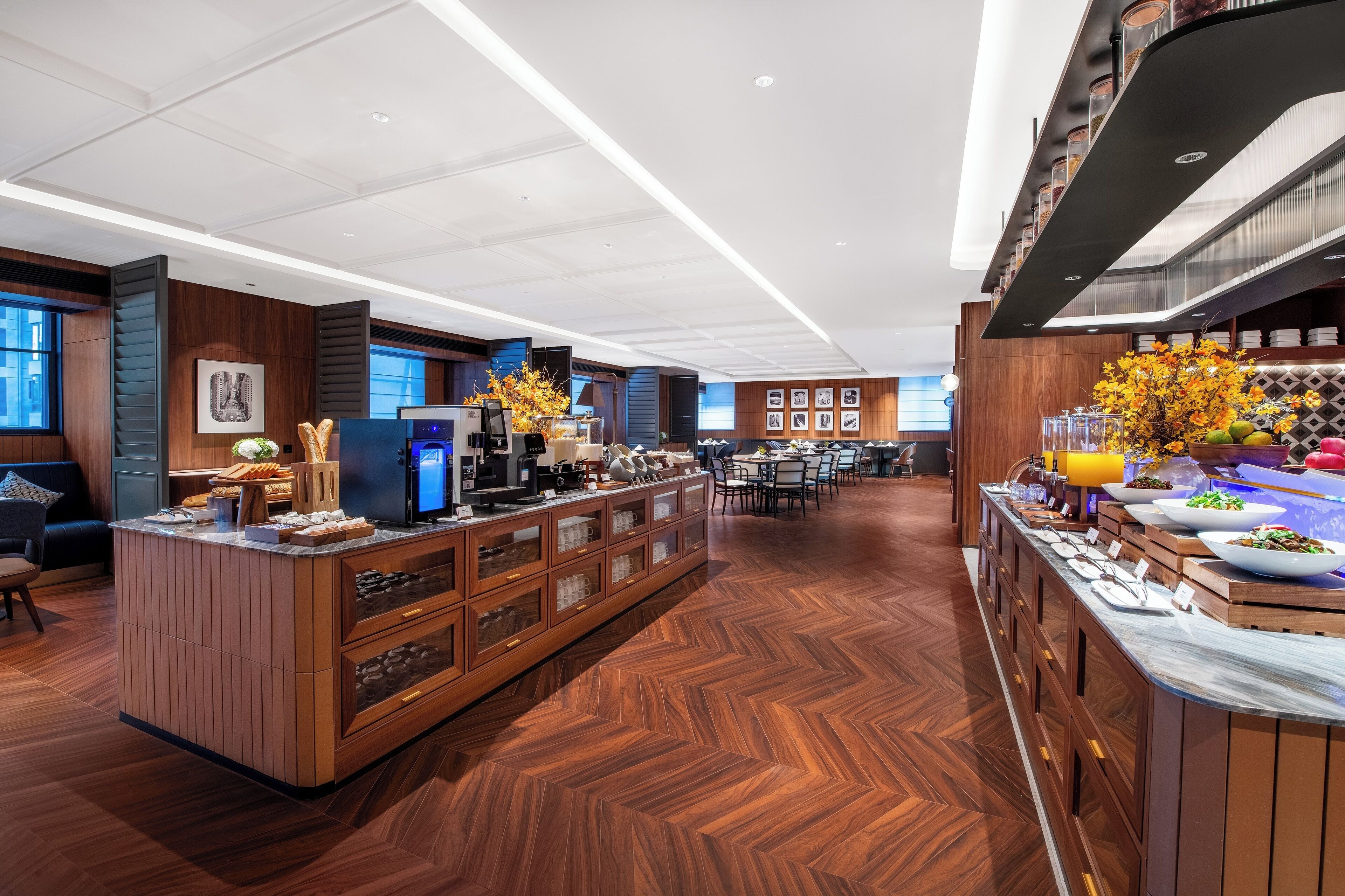 Um saguão de hotel moderno com uma ilha central, área de refeições e um buffet com diversos alimentos.
