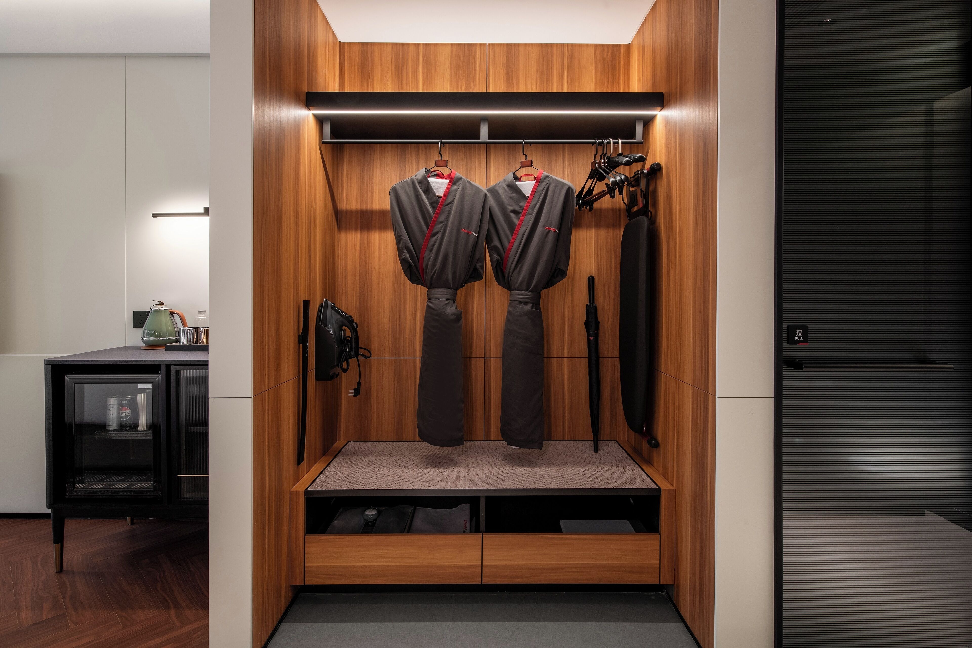 A modern locker room with wooden paneling, two hanging lockers, a bench, and a black door.