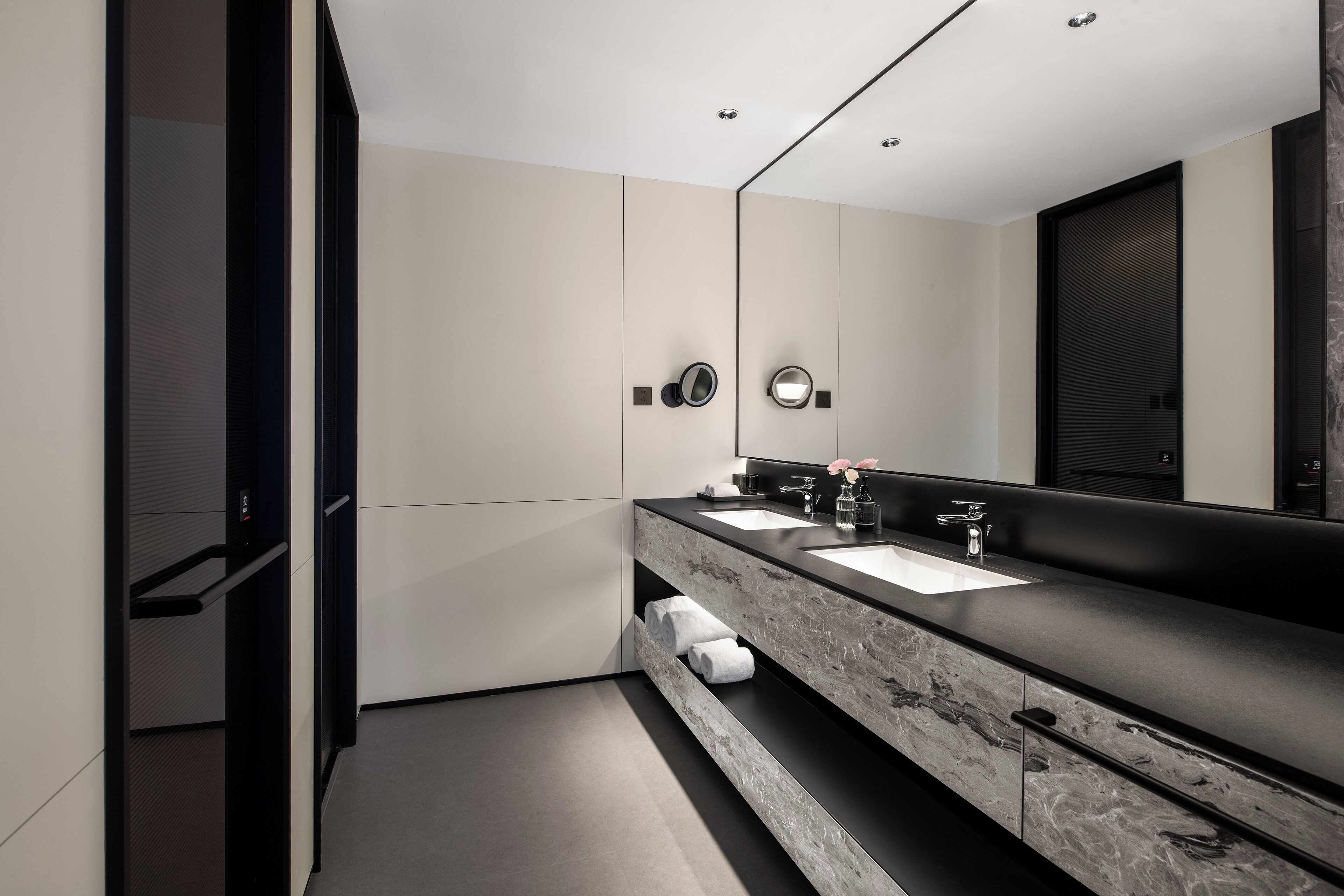 A modern bathroom with a long vanity, two sinks, a large mirror, and a towel rack.