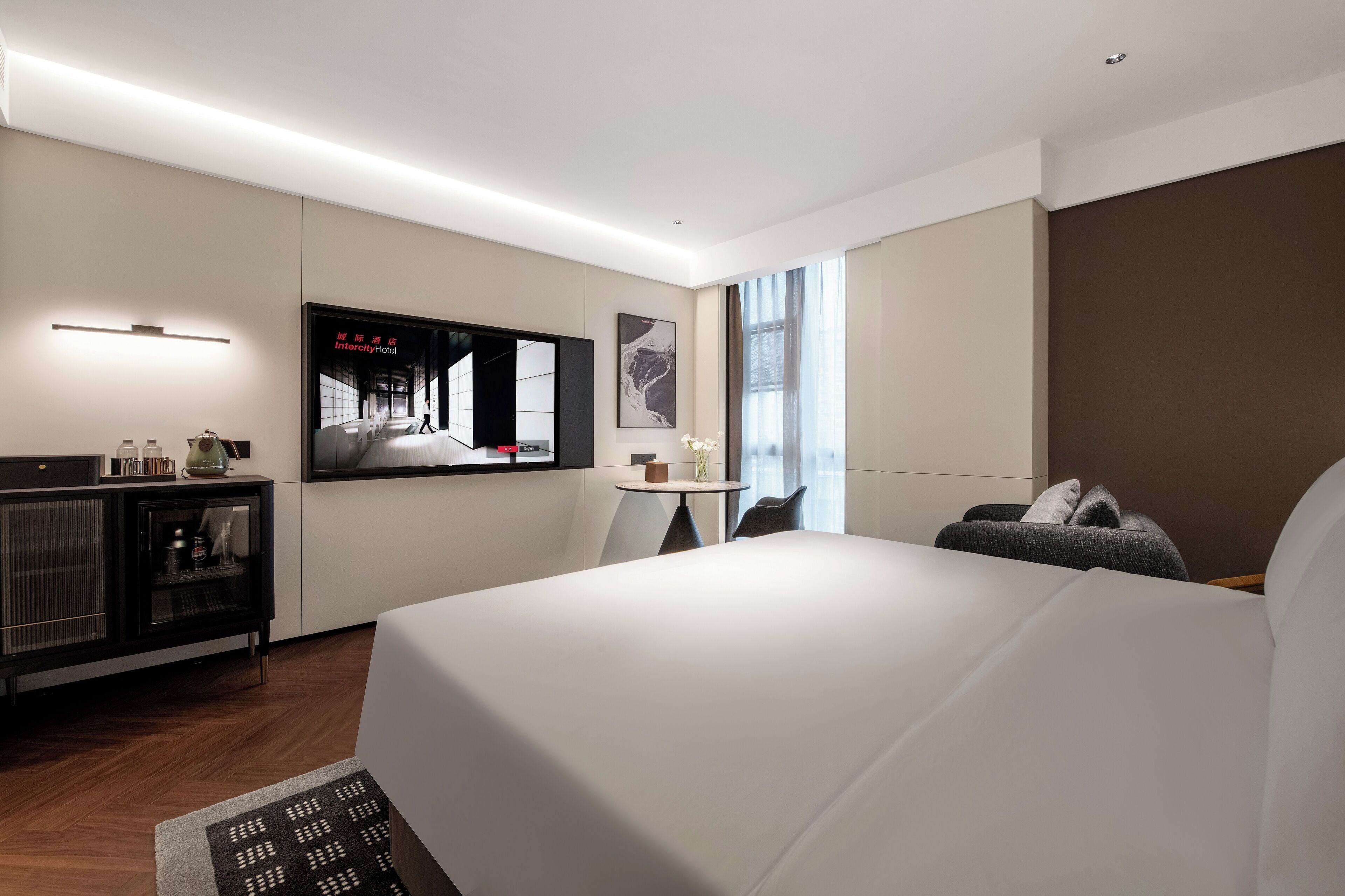 A modern hotel room with a large bed, a small desk, a television, and a window with curtains.