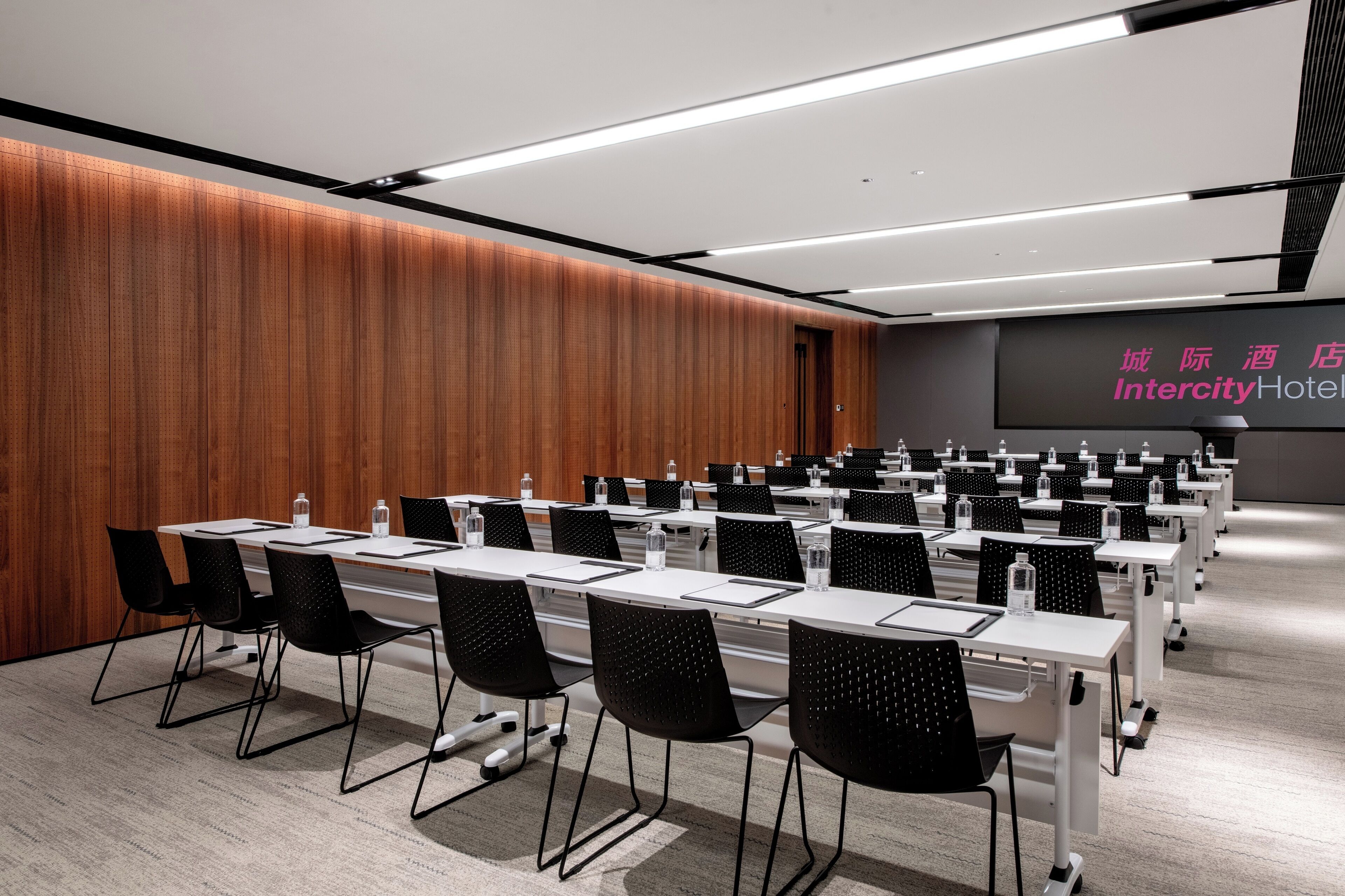 A conference room with multiple tables and chairs, a wooden wall, and a sign for Intercity Hotel.