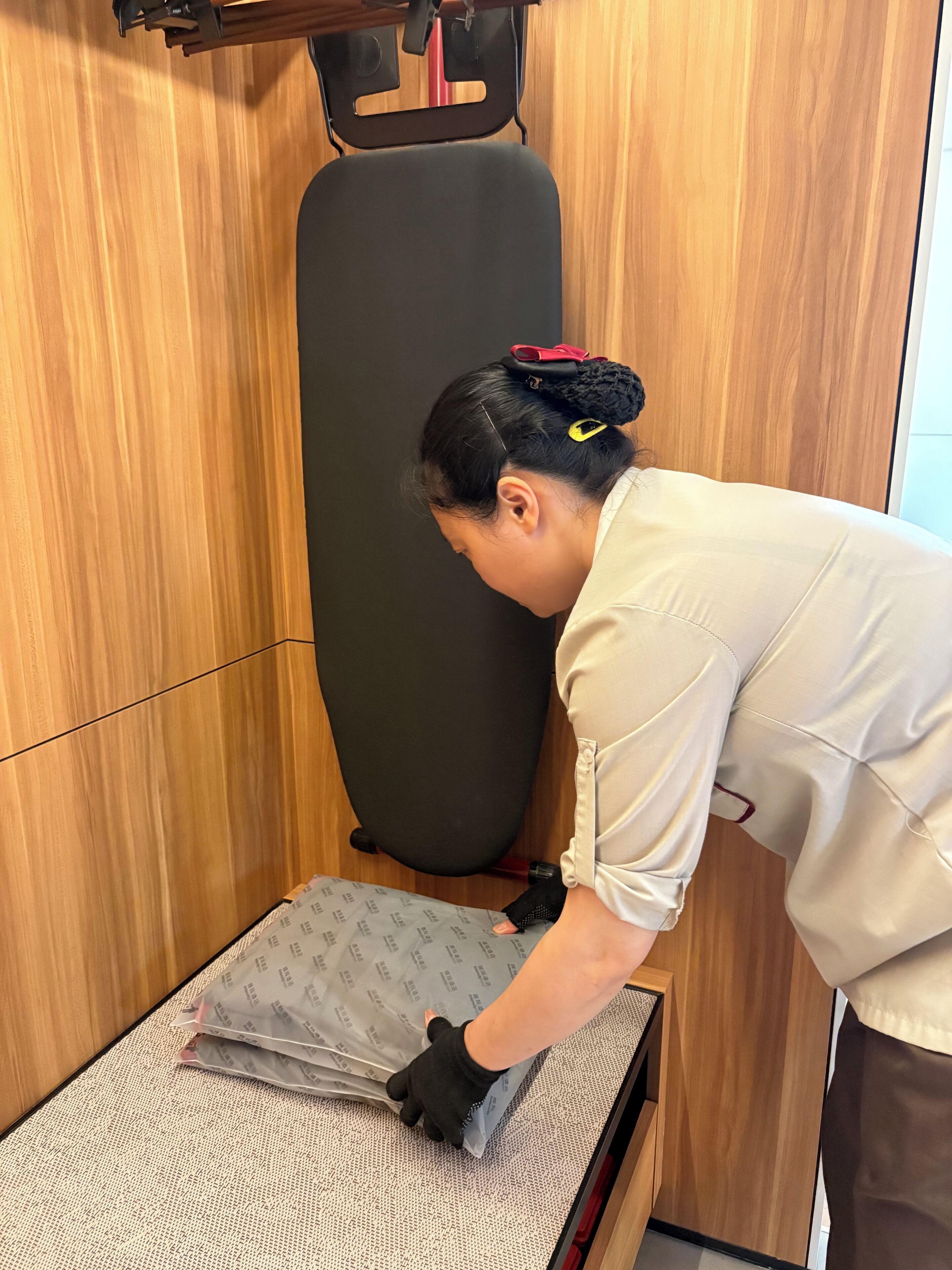 A person in a white shirt and black gloves handling a package on a textured surface in a room with wooden paneling.