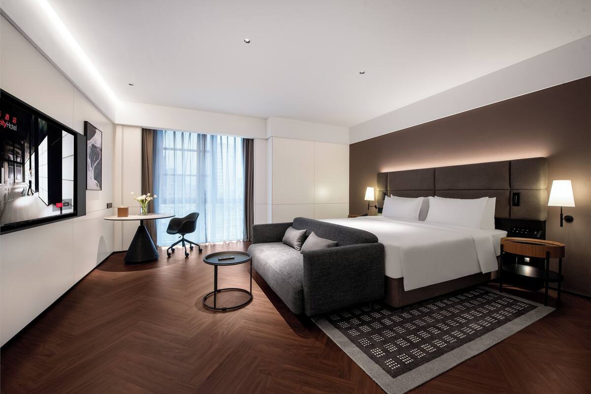 A modern hotel room with a bed, a sofa, a small table, and a desk.