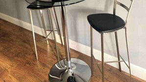 Un espace repas moderne avec une table ronde en verre, deux chaises en métal, une plante en pot et un téléviseur fixé au mur.