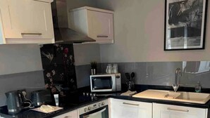 Une cuisine compacte avec des meubles blancs, un four à micro-ondes, une cuisinière et une table à manger avec un plateau en verre.