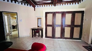 A room with a tiled floor, a red sofa, a small table, and a large wooden door with a woven screen. - Luxurious 3-Bedroom Holiday House with Pool Access in Diani Beach (Diani Beach)