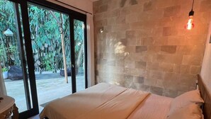 A bedroom with a bed, a nightstand, a hanging light fixture, and a view through a glass door to an outdoor area with greenery. - Cozy Villa El BamboG with a private pool (Blahbatuh)