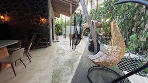 A patio area with a stone wall, a hanging chair, and a table with chairs. - Cozy Villa El BamboG with a private pool (Blahbatuh)