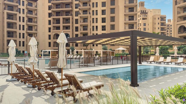 A poolside area with lounge chairs and umbrellas, surrounded by high-rise residential buildings. - StayShort - Modern 1BR Retreat in MJL Sleeps 4 (Madinat Jumeirah Living)