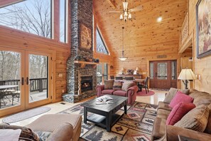 A spacious log cabin interior with a stone fireplace, wooden ceiling, and large windows. - Serene Creek Cabin w/ Fire Pit, Air Hockey, Pool Table, Yard, Pet Friendly ne... (Todd)