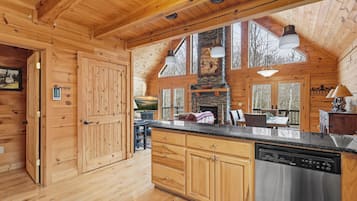 A wooden cabin interior with a kitchen, dining area, and a large window overlooking a deck.