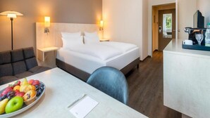 A hotel room with a bed, bedside tables, a desk with a fruit bowl, a chair, and a coffee machine. - Sunday Hotel Bielefeld Superior King Room (Bielefeld)