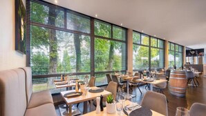 A modern restaurant with large windows, wooden tables, and comfortable seating. - Sunday Hotel Bielefeld Superior King Room (Bielefeld)