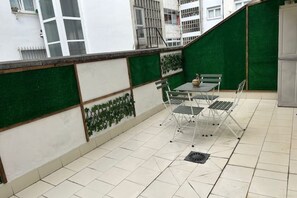 Eine Terrasse mit Tisch und Stühlen, eine grüne Wand mit Pflanzen und ein gefliester Boden.