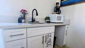Una cocina con armarios blancos, un lavamanos, un microondas y una cafetera.