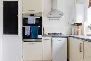 A kitchen with a black door, a stove, an oven, a dishwasher, and a white cabinet. - Peaceful 2BDR Flat in Serene Clapham Cul de Sac (London)